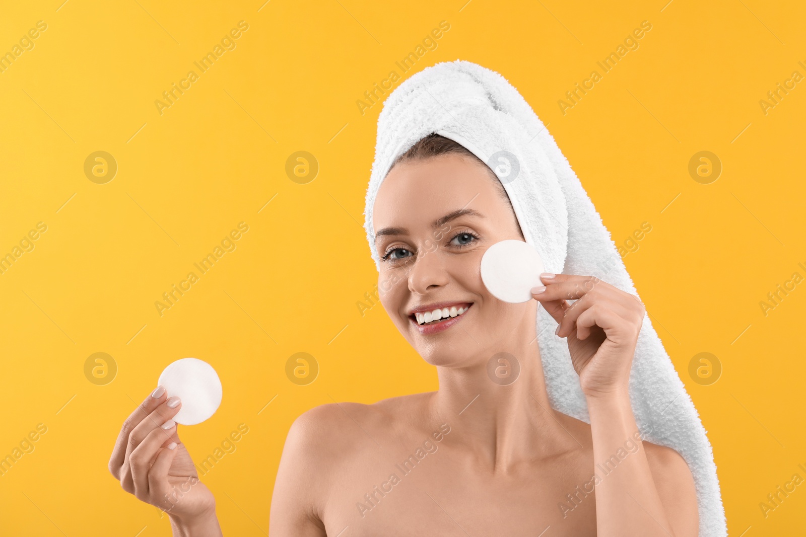 Photo of Removing makeup. Smiling woman with cotton pads on yellow background