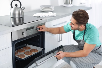 Young man baking cookies in oven at home