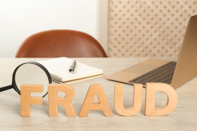 Photo of Word Fraud made of wooden letters near laptop and magnifying glass on office desk. Space for text