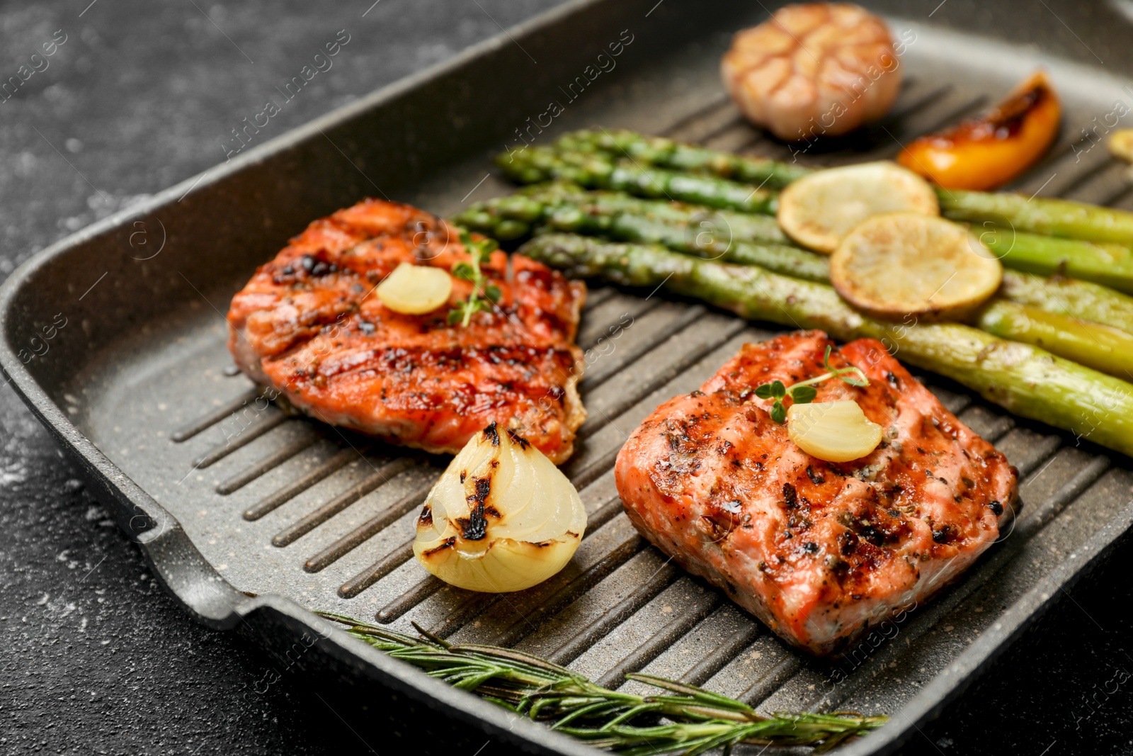 Photo of Frying pan with tasty grilled salmon, lemon and asparagus on black table, closeup