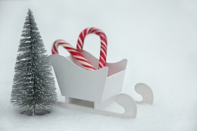 Photo of White wooden sleigh with candy canes and decorative fir tree on snow outdoors