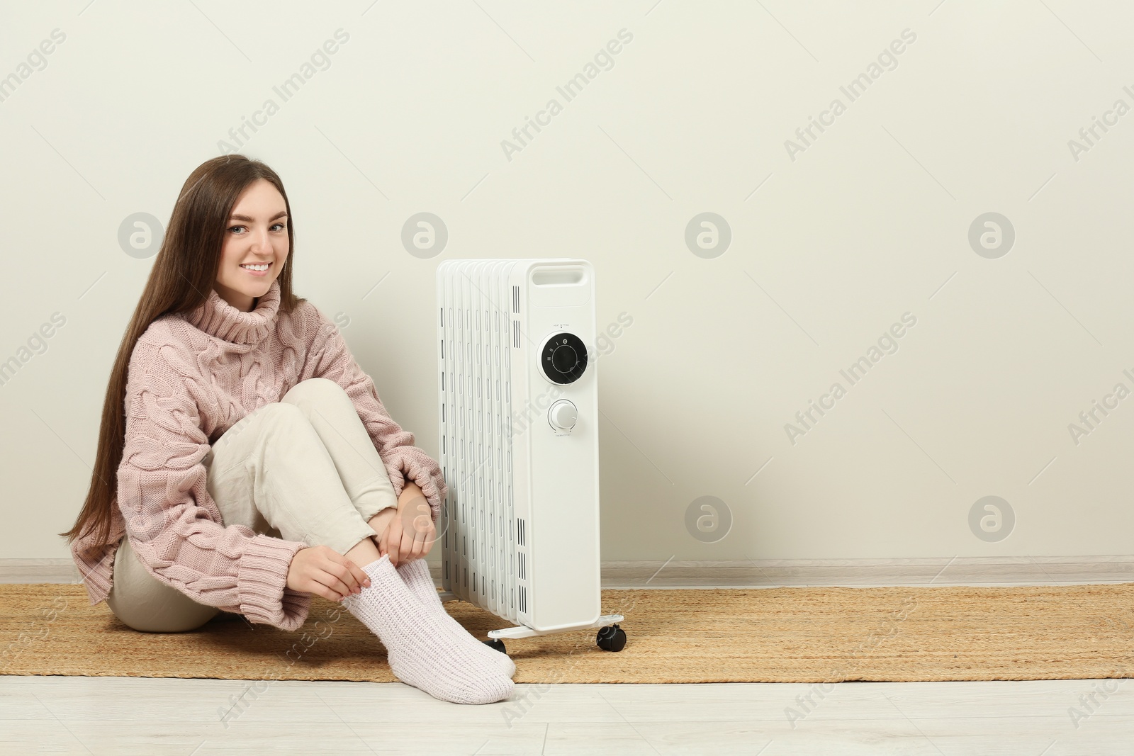 Photo of Young woman warming herself near modern electric heater indoors, space for text