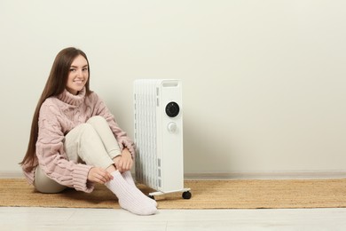 Young woman warming herself near modern electric heater indoors, space for text