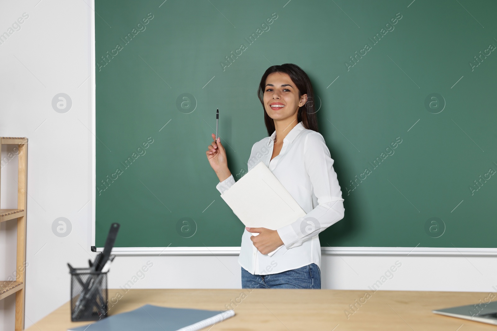 Photo of Happy young teacher giving lesson at blackboard in classroom. Space for text