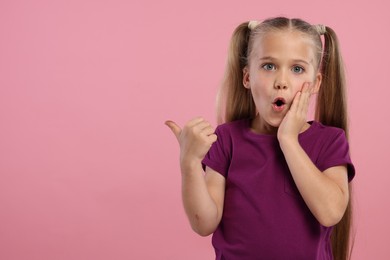 Photo of Special promotion. Emotional little girl pointing at something on pink background. Space for text