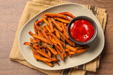 Photo of Sweet tasty potato fries and ketchup served on wooden table, top view