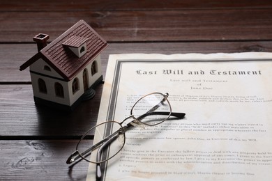 Photo of Last Will and Testament, house model and glasses on wooden table, closeup