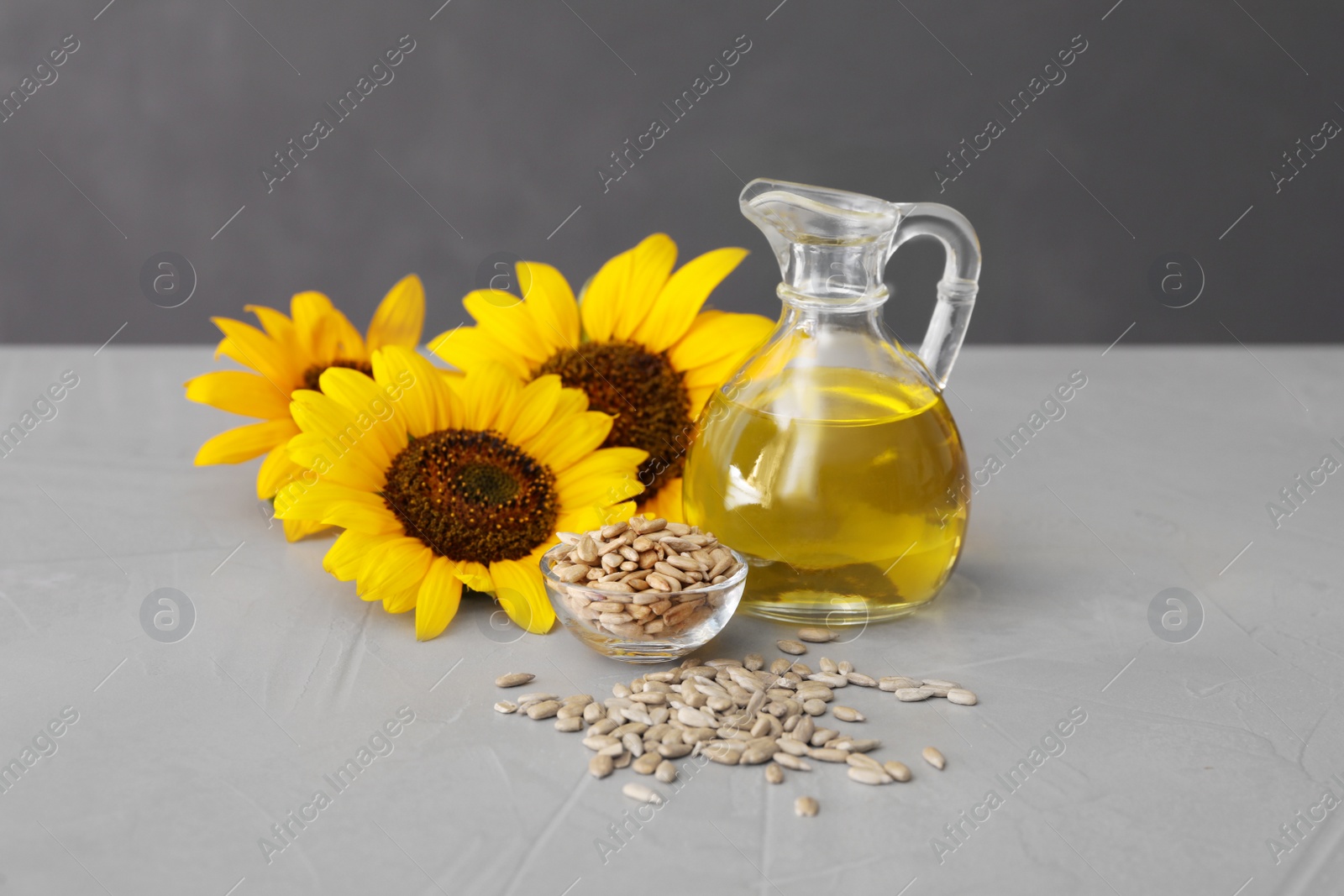 Photo of Sunflowers, jug of oil and seeds on grey table