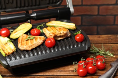 Photo of Electric grill with tasty meat, rosemary and vegetables on wooden table