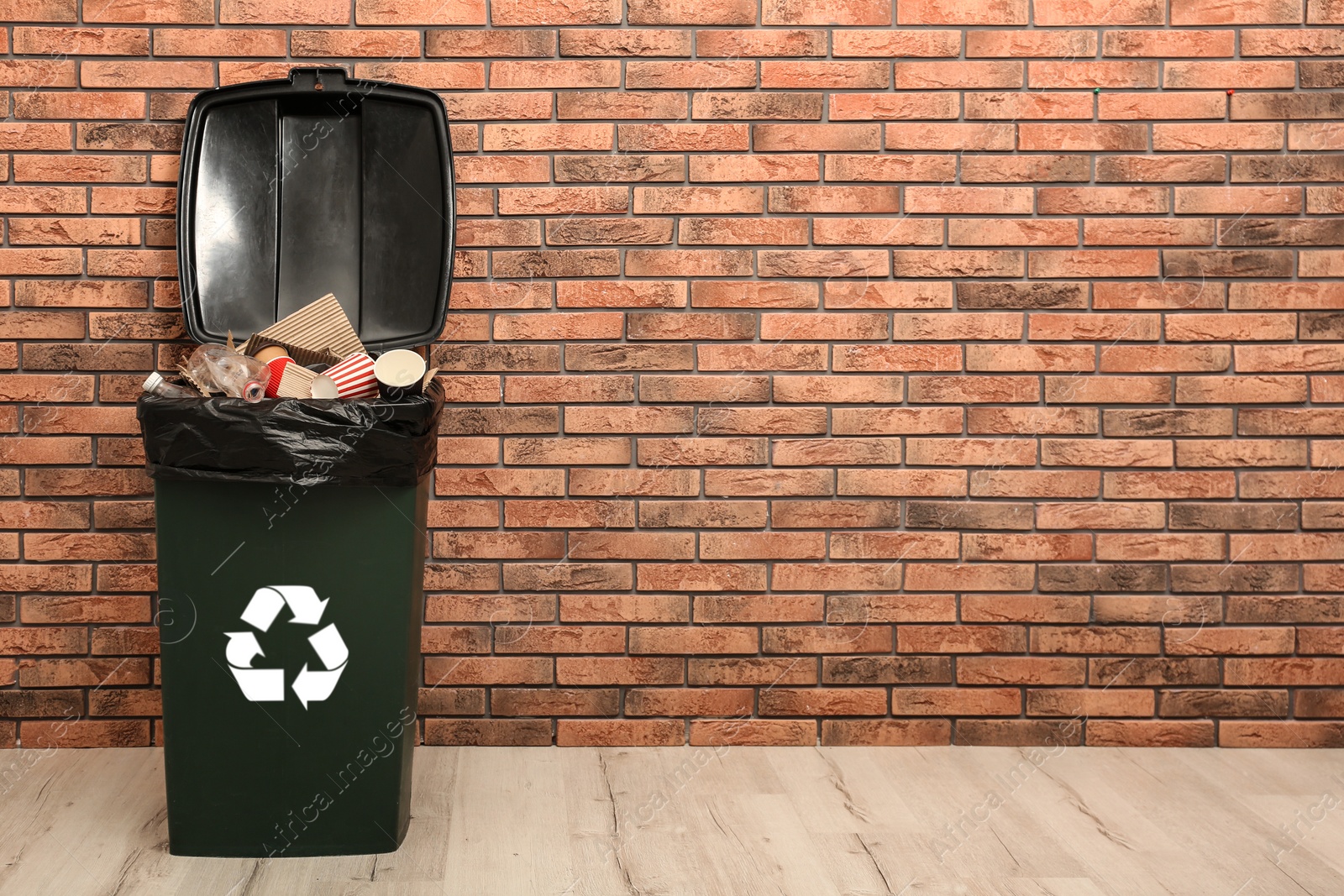 Photo of Full trash bin near brick wall indoors, space for text. Waste recycling
