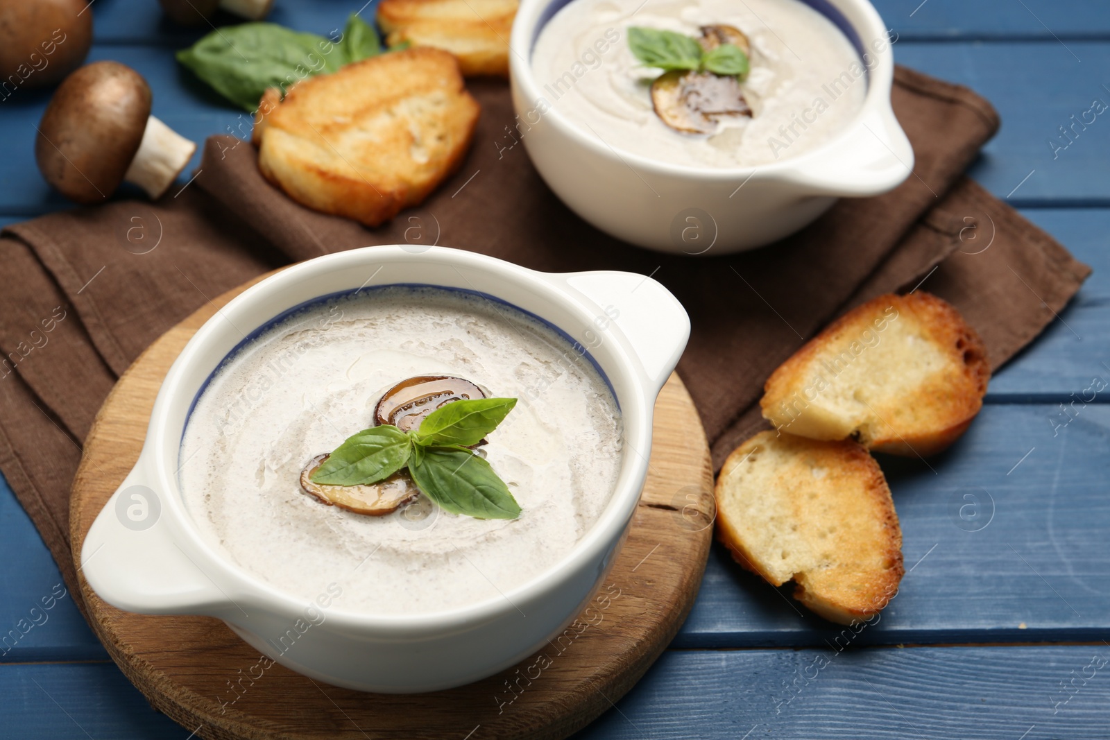 Photo of Fresh homemade mushroom soup ceramic pots on blue wooden table