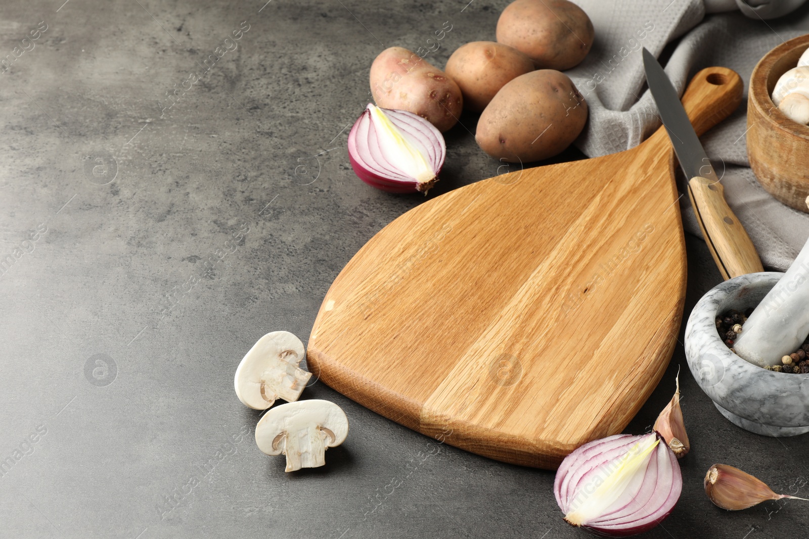 Photo of Wooden cutting board and products on dark textured table. Space for text