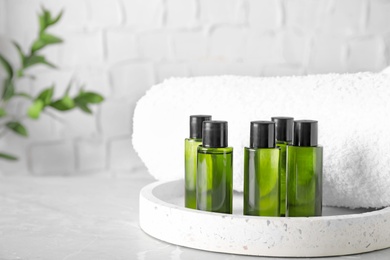 Mini bottles with cosmetic products and towel on grey marble table against light background. Space for text