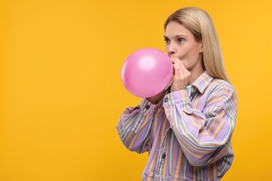 Photo of Woman blowing up balloon on yellow background. Space for text