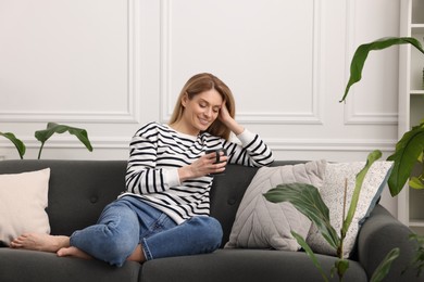 Photo of Woman with cup of drink sitting on sofa surrounded by beautiful potted houseplants at home