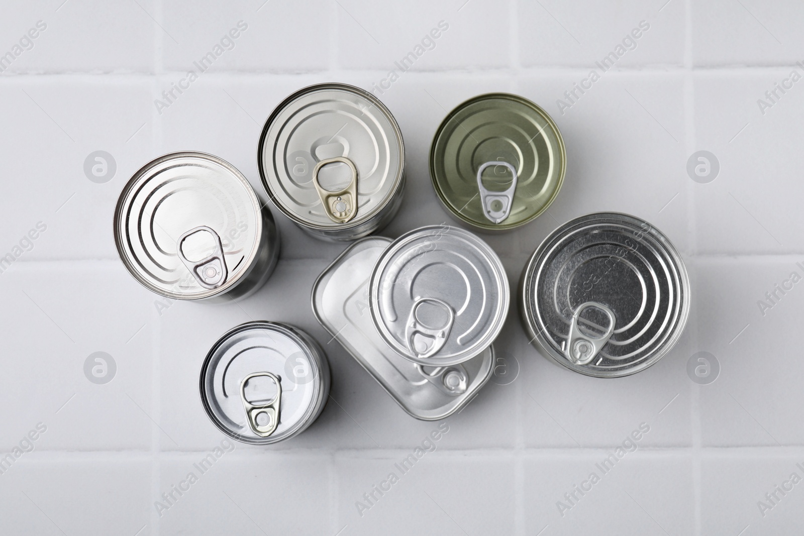 Photo of Many closed tin cans on white tiled table, flat lay