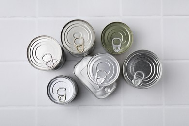 Photo of Many closed tin cans on white tiled table, flat lay