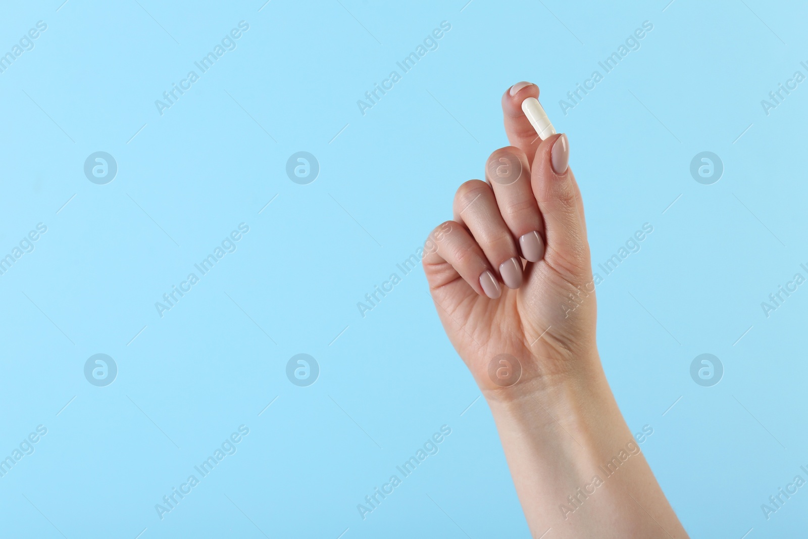 Photo of Woman holding vitamin capsule on light blue background, closeup with space for text. Health supplement