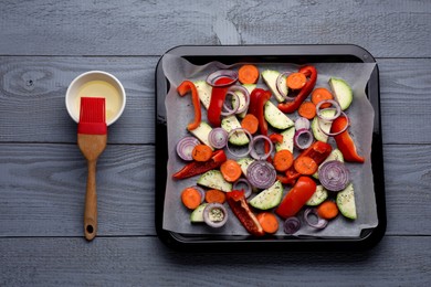 Baking pan with parchment paper and raw vegetables on grey wooden table, flat lay