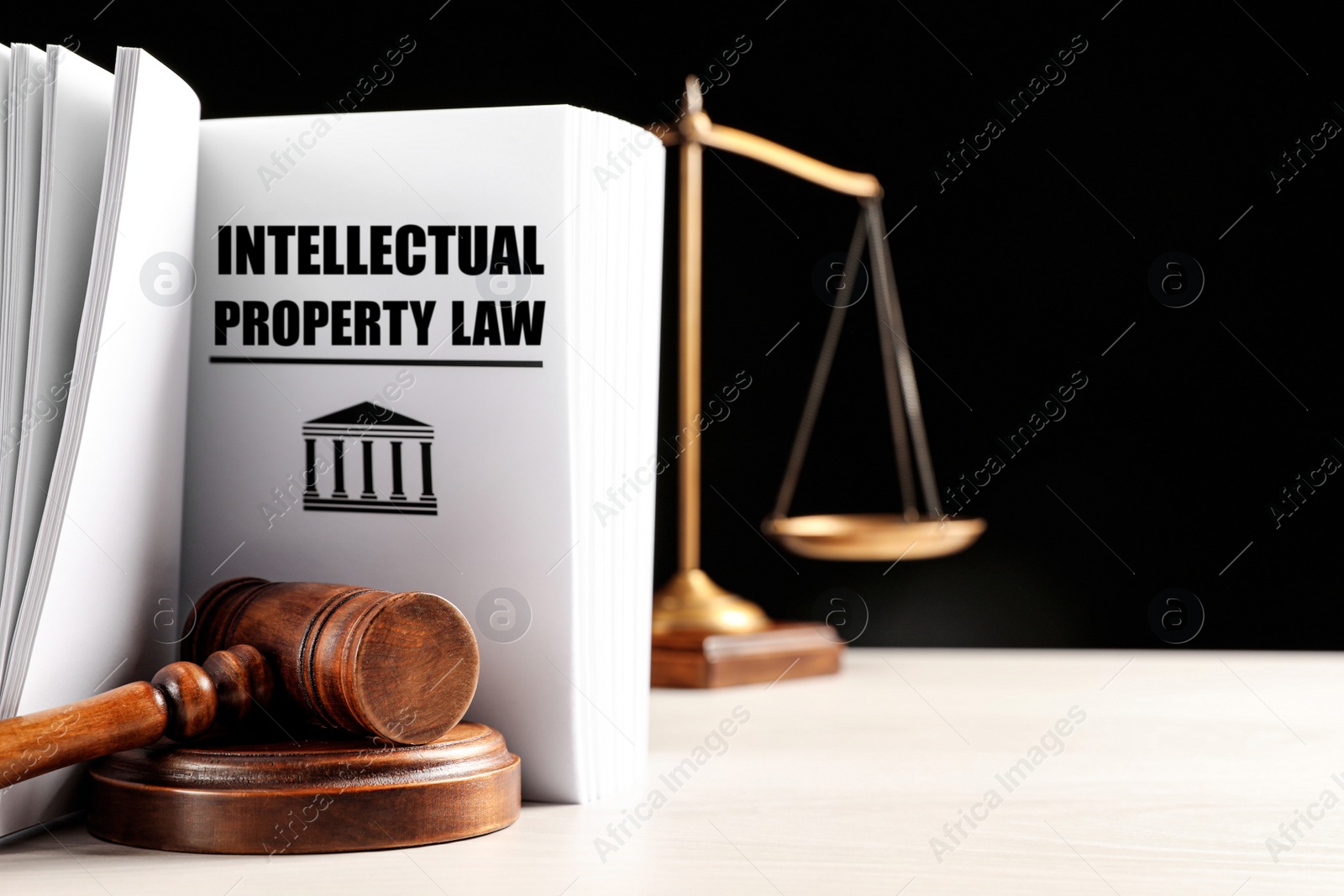 Image of Intellectual Property law book, judge's gavel and scales of justice on white table against black background. Space for text