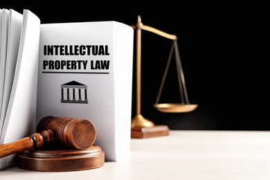 Image of Intellectual Property law book, judge's gavel and scales of justice on white table against black background. Space for text