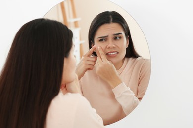 Photo of Young woman squeezing pimple near mirror indoors. Hormonal disorders