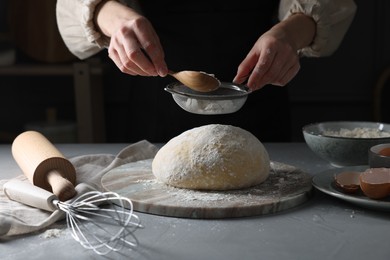 Photo of Making dough. Woman sifting flour at grey table, closeup