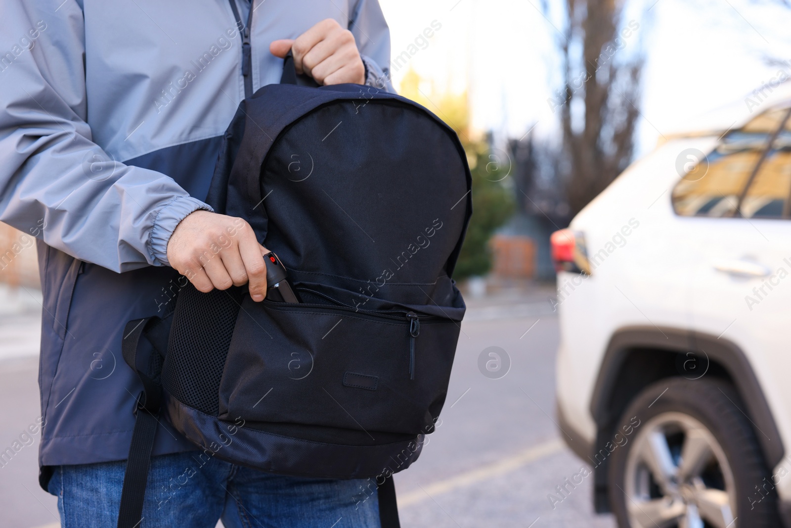 Photo of Man putting pepper spray into backpack outdoors, closeup. Space for text