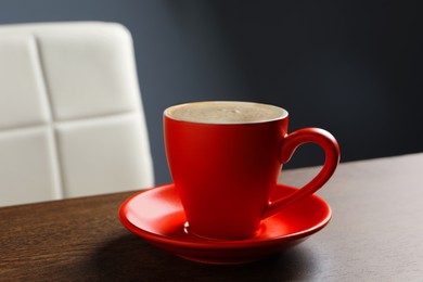Photo of Red cup with cappuccino on wooden table indoors