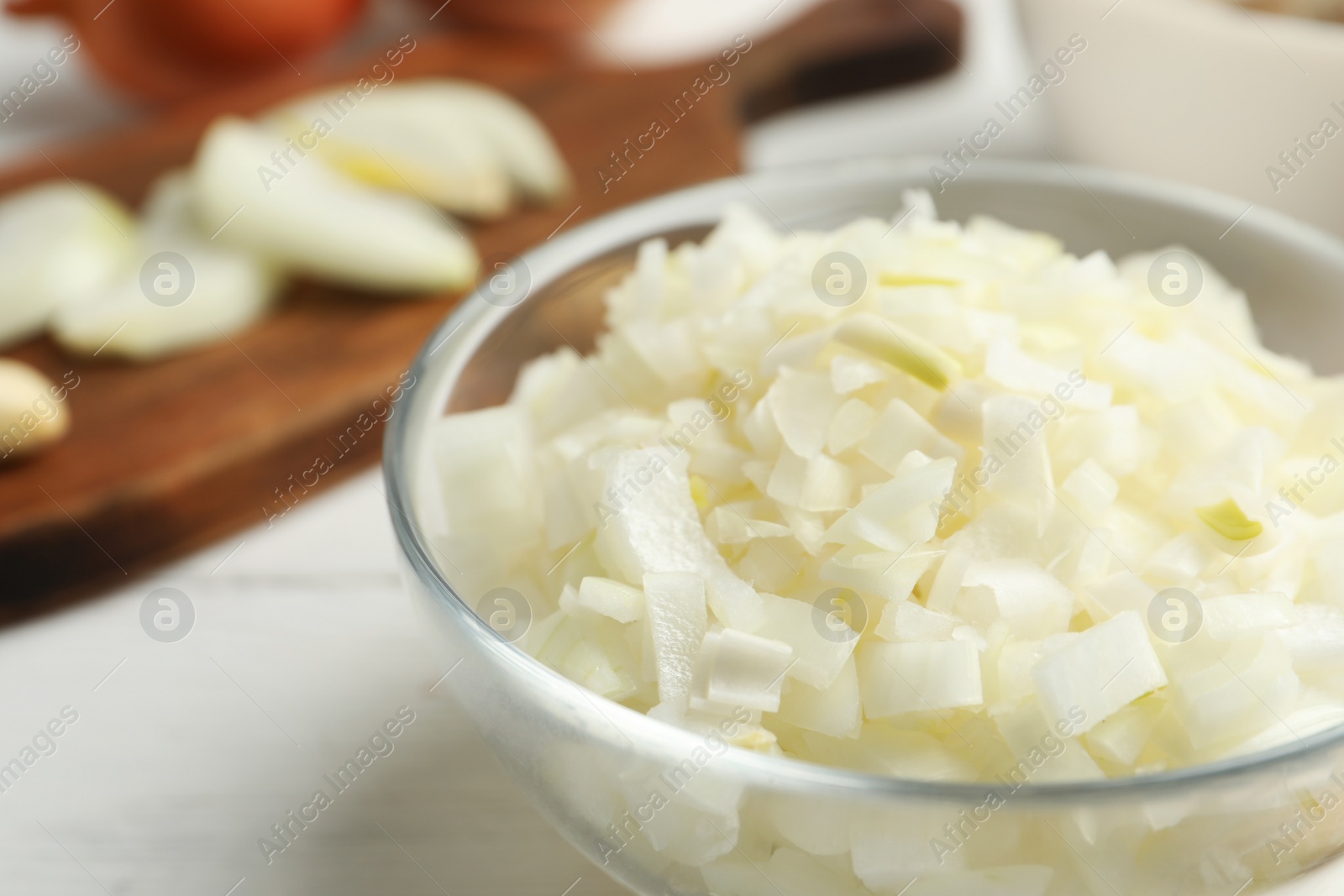 Photo of Chopped onion in bowl on white wooden table, closeup