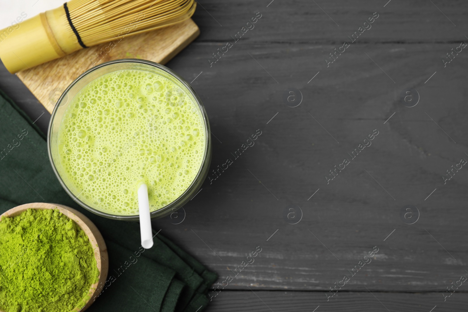 Photo of Glass of tasty matcha smoothie, powder and bamboo whisk on grey wooden table, flat lay. Space for text