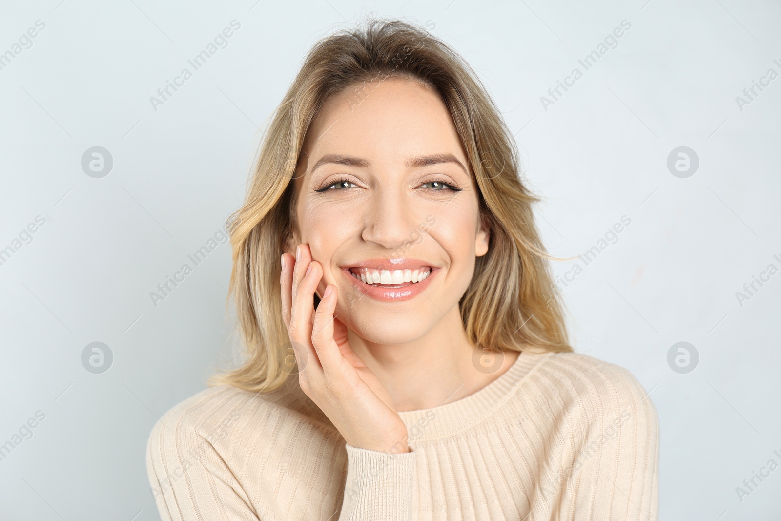 Photo of Portrait of happy young woman with beautiful blonde hair and charming smile on light background