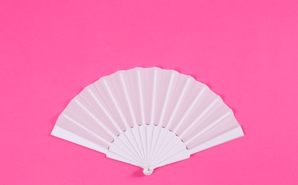 White hand fan on pink background, top view