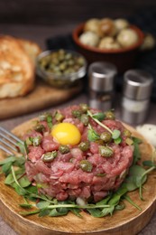 Photo of Tasty beef steak tartare served with yolk, capers and microgreens on serving board