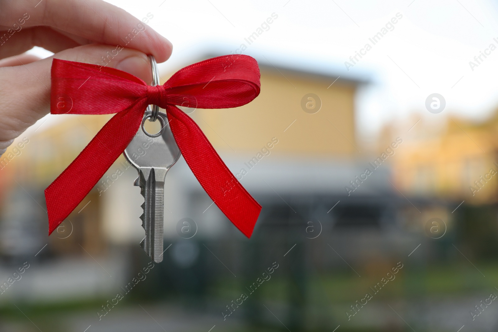 Photo of Woman holding key with bow near house outdoors, closeup. Space for text