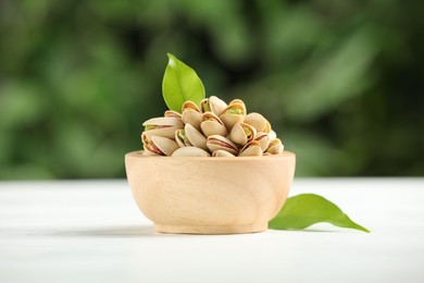 Photo of Tasty pistachios in bowl on white wooden table against blurred background, closeup