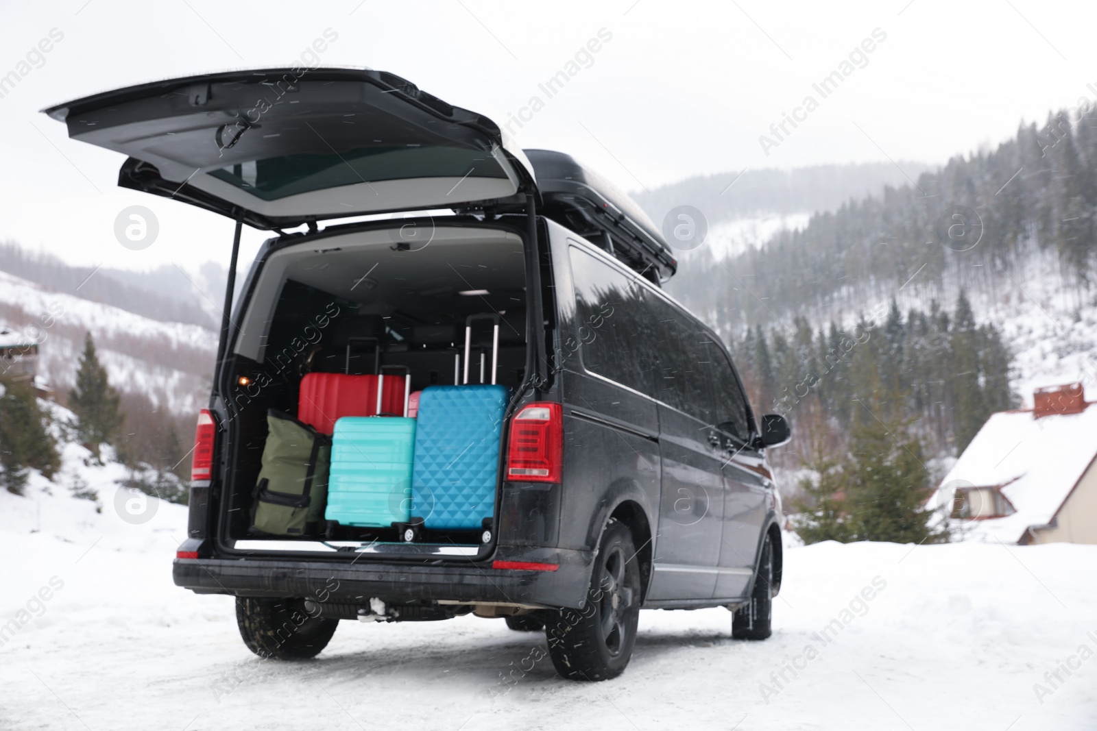 Photo of Black car with luggage in trunk on snowy road. Winter vacation