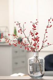 Hawthorn branches with red berries in vase on table indoors