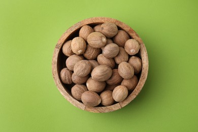 Photo of Whole nutmegs in bowl on light green background, top view