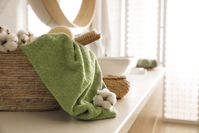 Photo of Wicker basket with clean towel, massage brush and cotton flowers on countertop in bathroom. Space for text