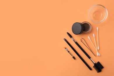 Photo of Eyebrow pomade with henna effect and professional tools on orange background, flat lay. Space for text