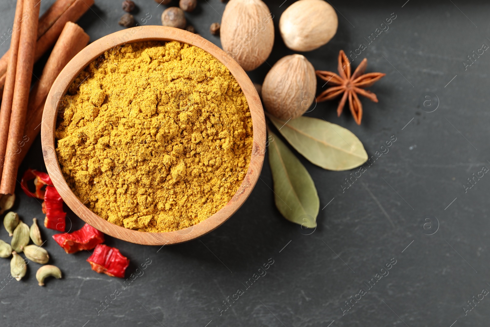 Photo of Dry curry powder in bowl and other spices on dark textured table, flat lay. Space for text