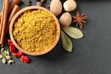 Dry curry powder in bowl and other spices on dark textured table, flat lay. Space for text