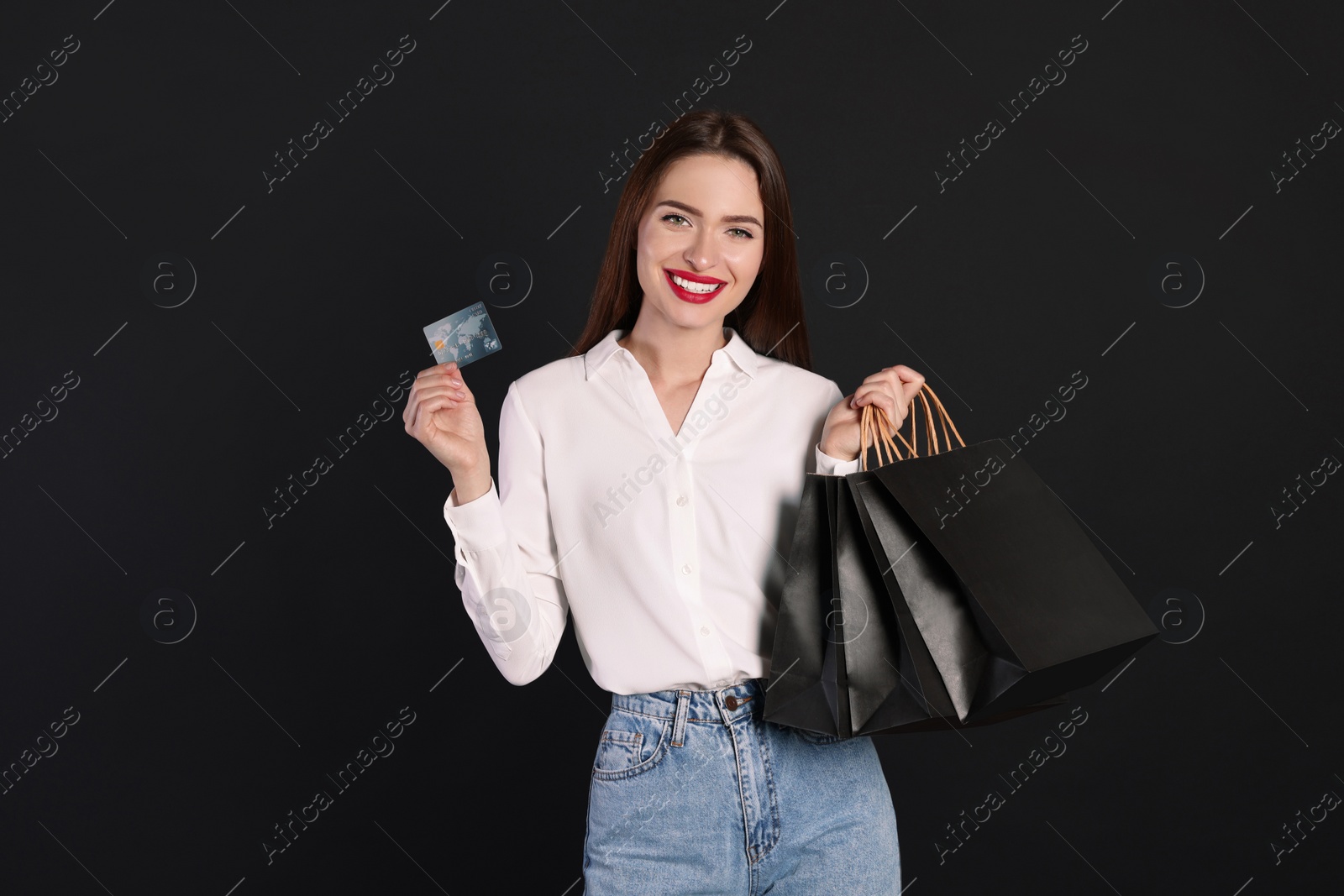 Photo of Happy young woman with shopping bags and credit card on black background. Big sale