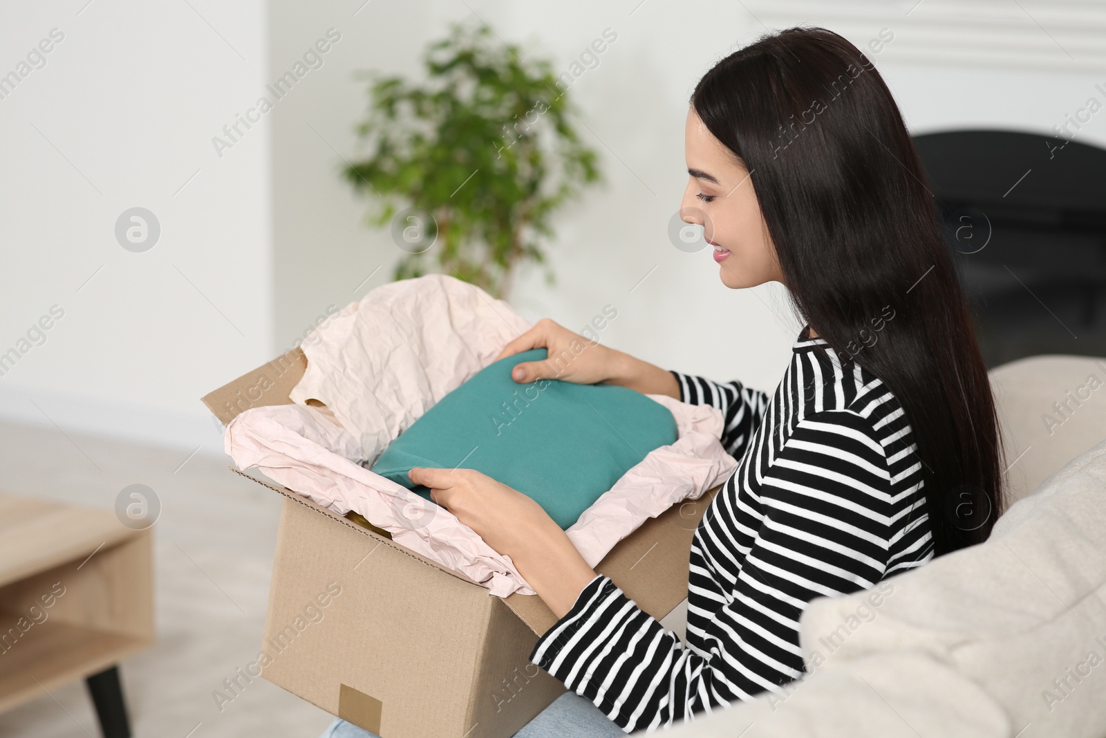 Photo of Happy young woman with parcel at home. Internet shopping