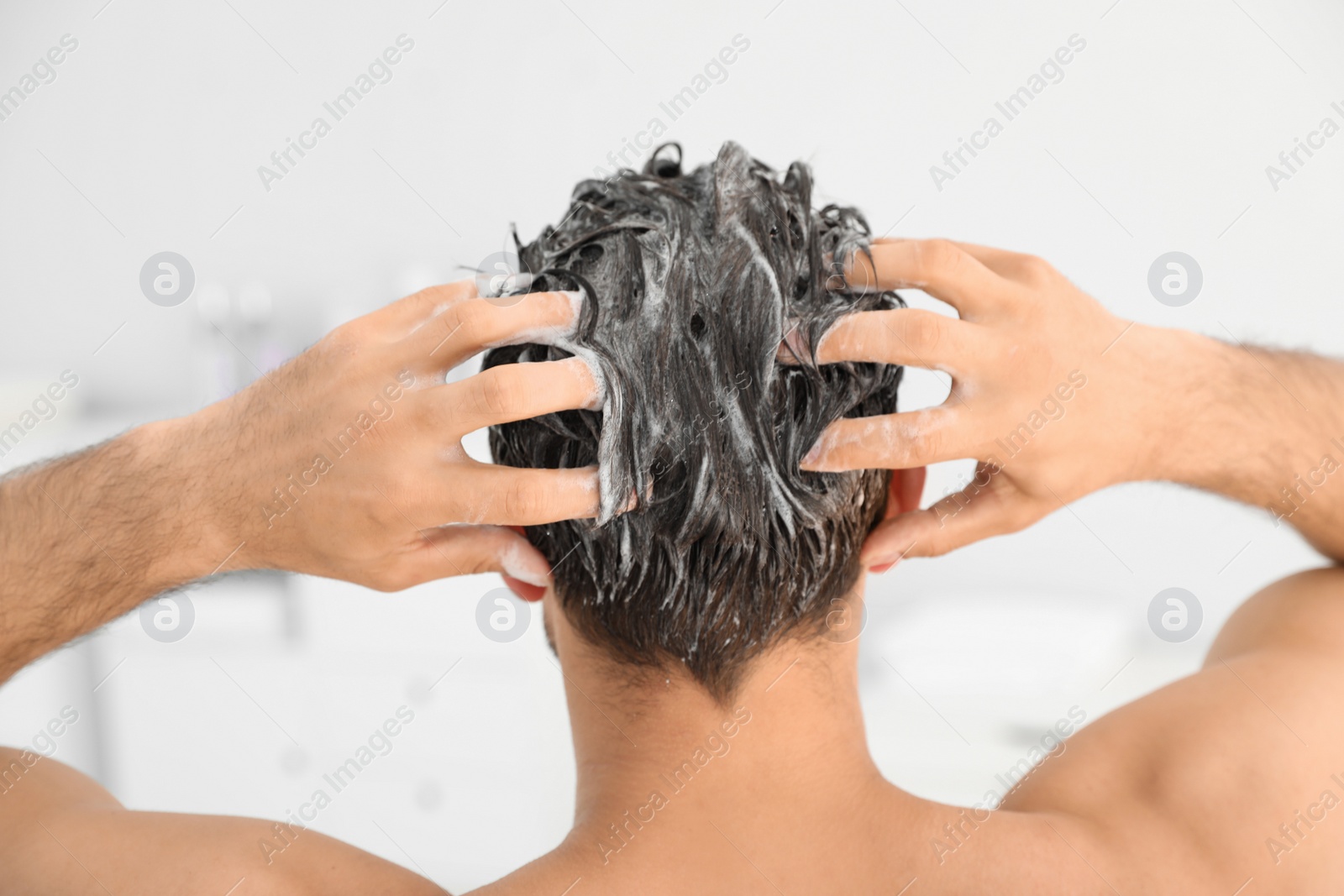 Photo of Man applying shampoo onto his hair against light background