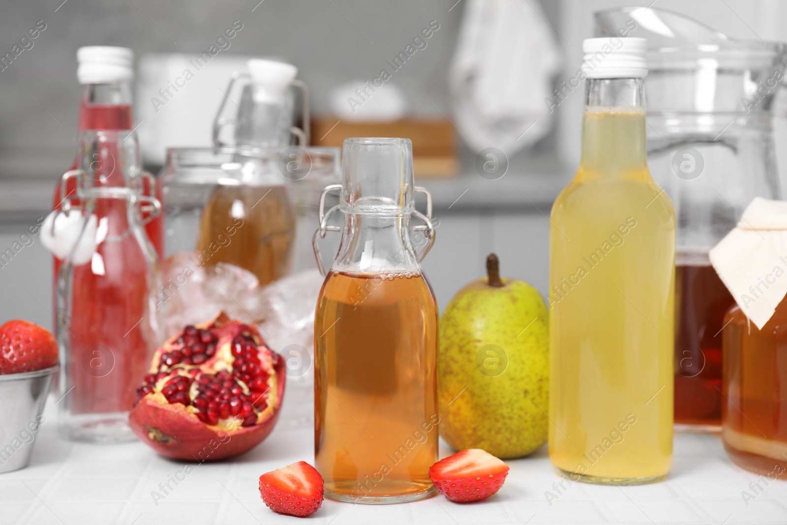 Photo of Tasty kombucha in glass bottles and fresh fruits on white tiled table