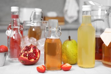 Tasty kombucha in glass bottles and fresh fruits on white tiled table