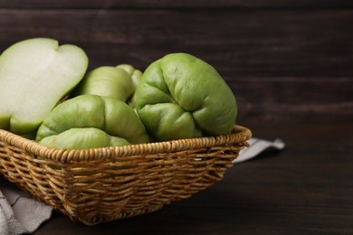 Photo of Cut and whole chayote in wicker basket on wooden table, closeup