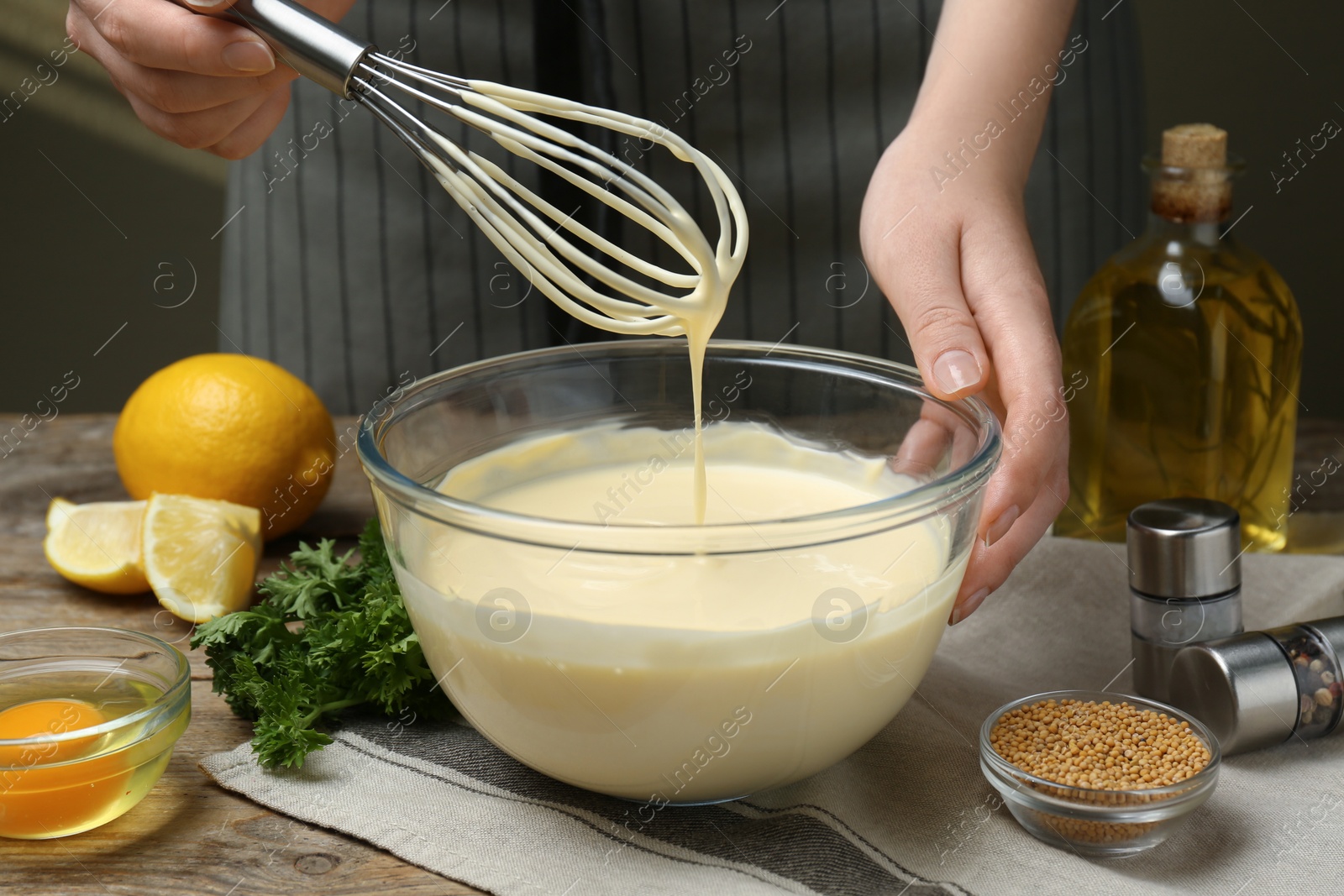 Photo of Woman making homemade mayonnaise in glass bowl at wooden table, closeup